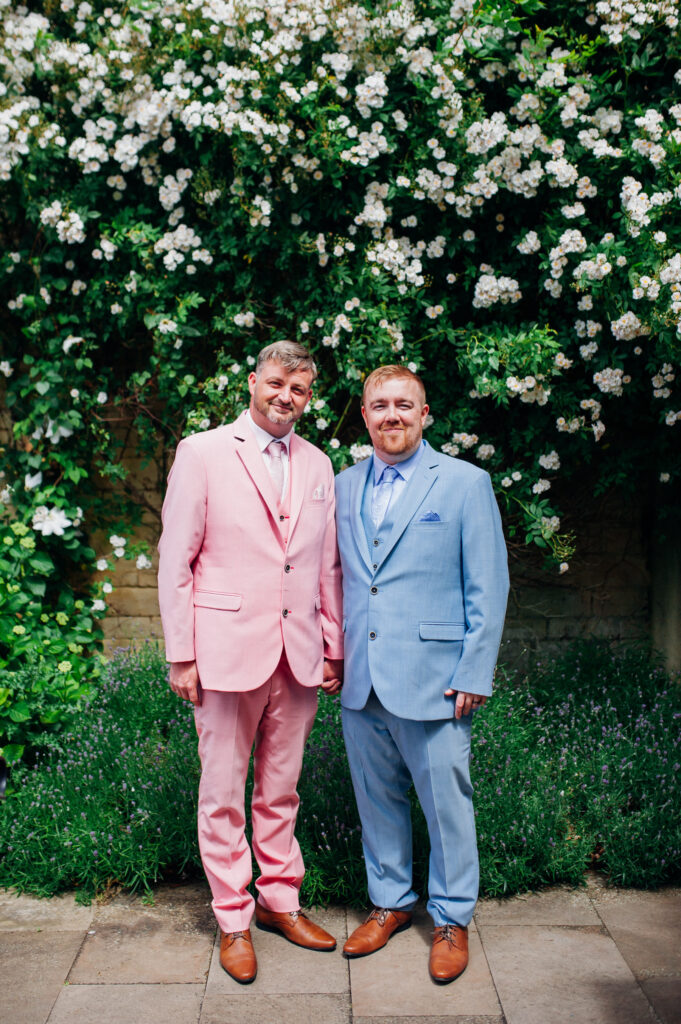 Tom (in the pink suit) and Ben (in the blue suit), founders of TPHN Digital Solutions, smiling on their wedding day.
